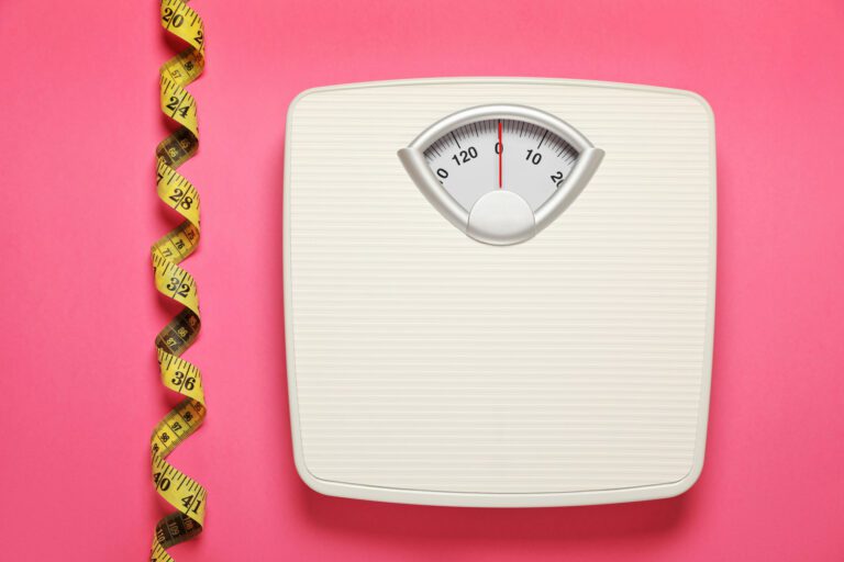 Weighing scales and measuring tape on pink background, flat lay.