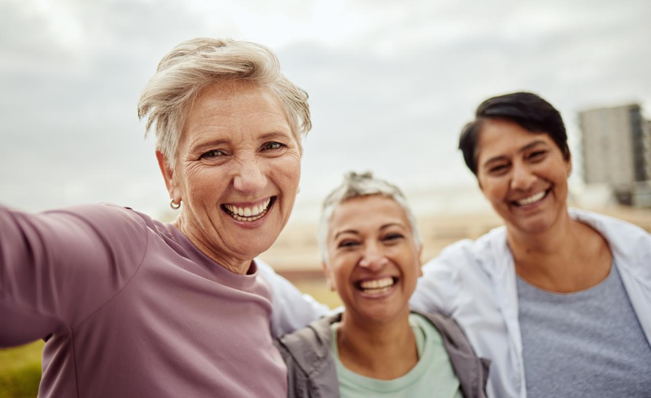 Three women smiling together outdoors, confident and vibrant