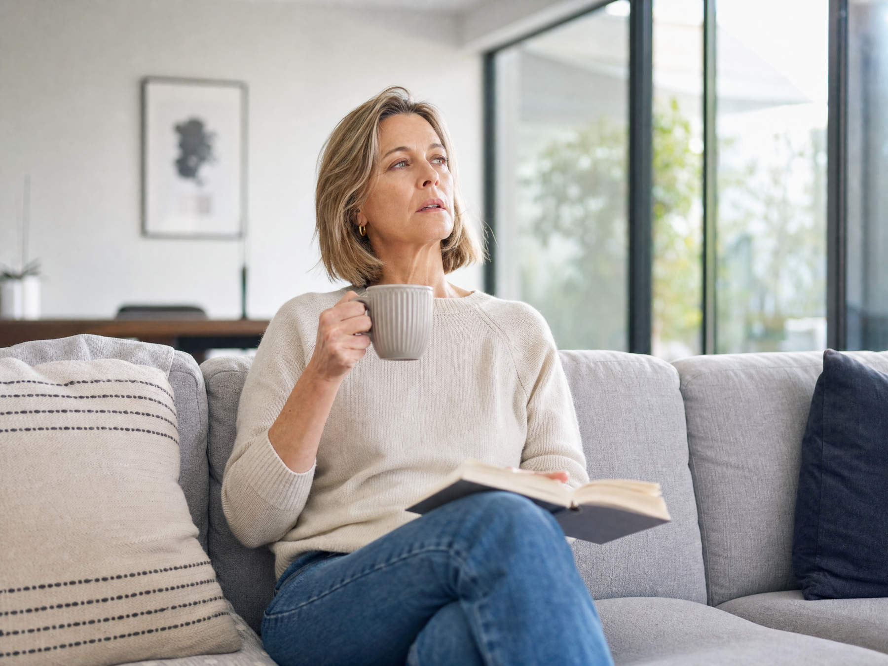 Woman in her 50s working thoughtfully at a laptop with tea, soft window light